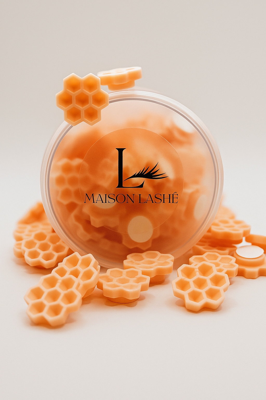 Maison Lashé honeycomb glue cup in transparent container surrounded by orange honeycomb-shaped glue cups on light beige background
