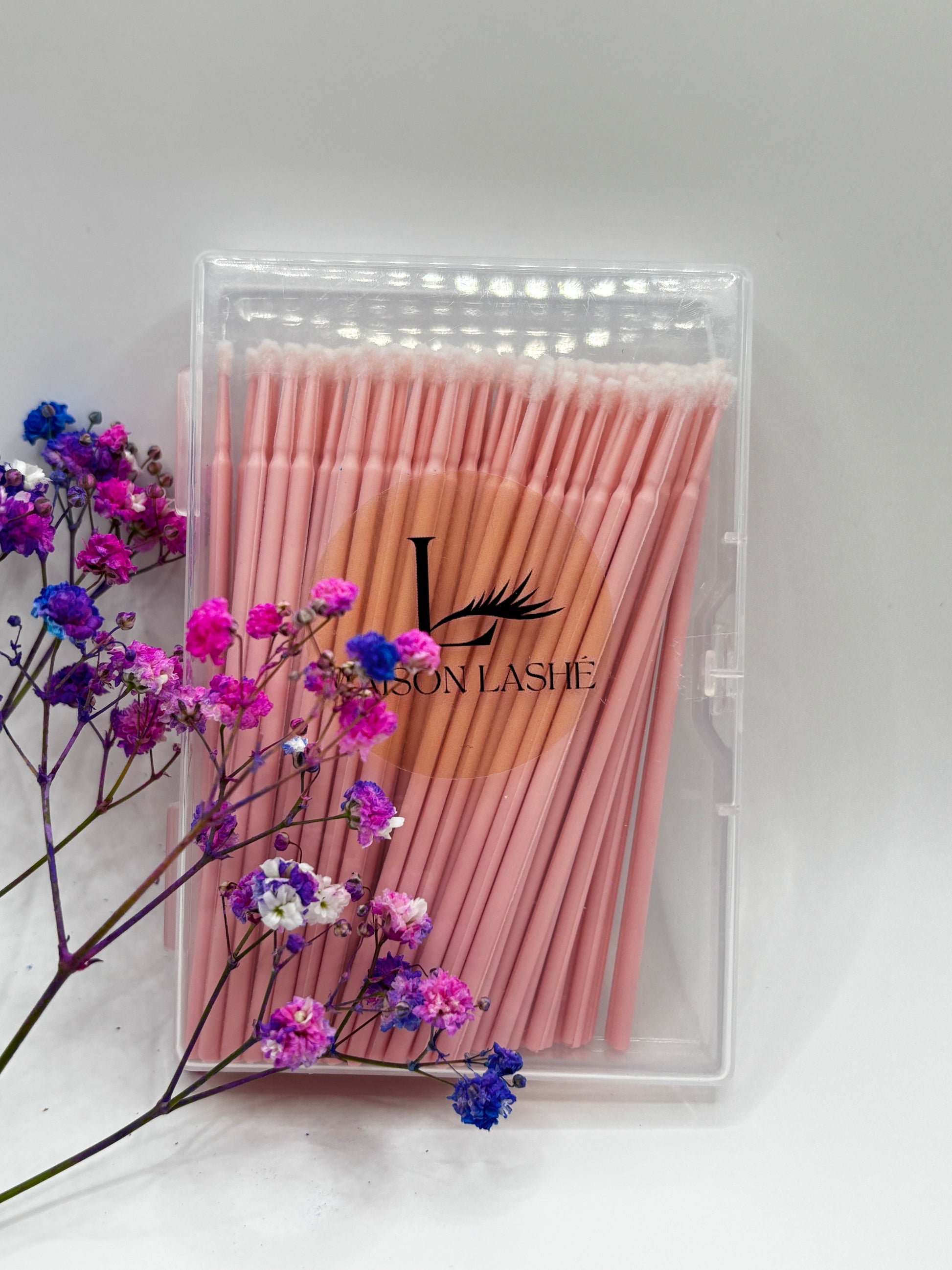 Maison Lashé microfibre brushes 100pcs packaged in a clear case with pink brushes and decorative flowers on a white background